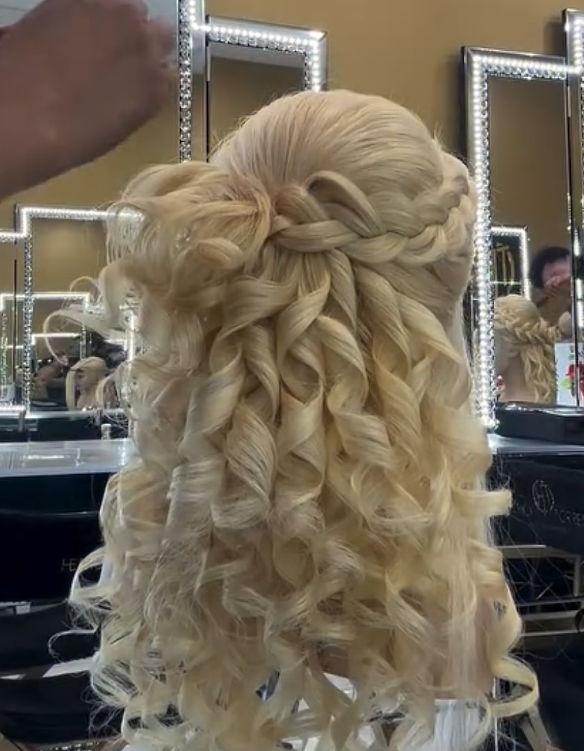 Un peinado rubio de medio recogido con corona de trenza y rizos en cascada, para evento.